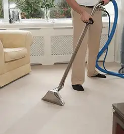 Professional carpet cleaner using a hot-water extraction wand and hose machine in a living room in Tallahassee, FL.
