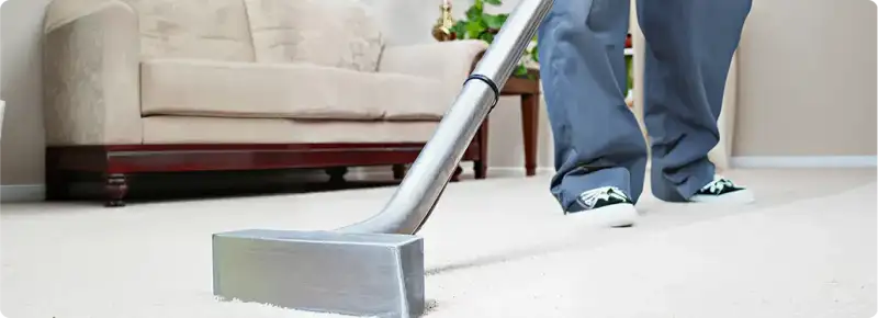 Carpet cleaning technician using a hot-water extraction wand on a light-colored carpet in a living room, Tallahassee, FL.