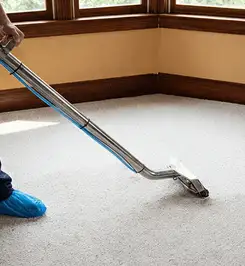 Steam carpet cleaning technician using a hot-water extraction wand on a residential carpet, wearing blue protective shoe covers Tallahassee, FL.