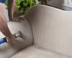 Professional upholstery cleaner deep-cleaning a fabric sofa with a handheld extraction tool and hose in Tallahassee, FL.